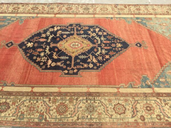 Terracotta and navy rug with a bold geometric center medallion and detailed floral borders on a stone floor.