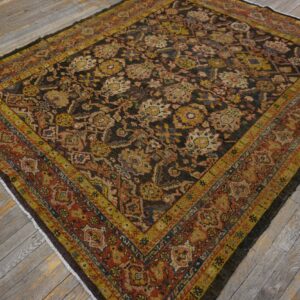 Black and brown rug with dense floral patterns and bold yellow-gold and rust-red borders on weathered wooden flooring.