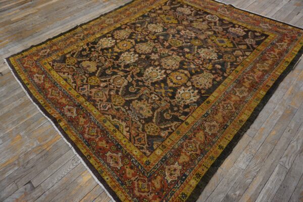 Black and brown rug with dense floral patterns and bold yellow-gold and rust-red borders on weathered wooden flooring.