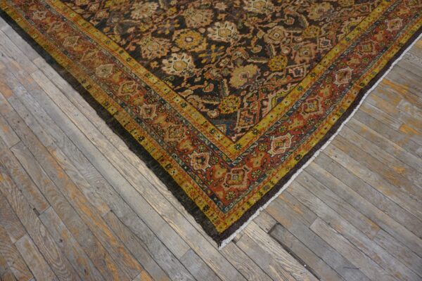 A dark, intricately patterned rug with gold and rust borders lies on weathered gray wood flooring.