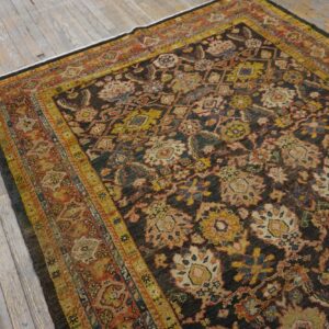 Dark brown traditional rug with dense yellow, rust, and blue floral motifs laid on aged wood floorboards.