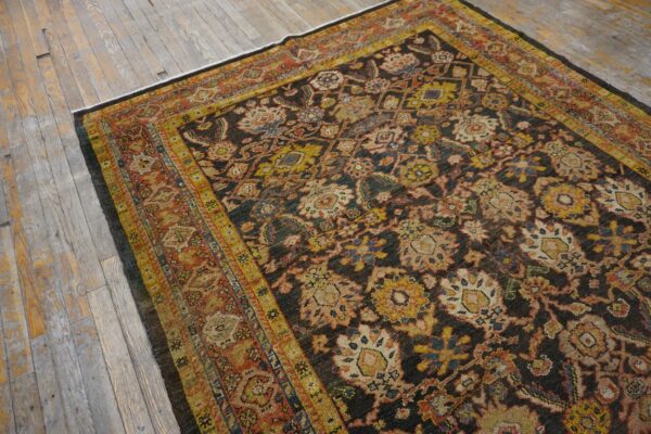 Dark brown traditional rug with dense yellow, rust, and blue floral motifs laid on aged wood floorboards.