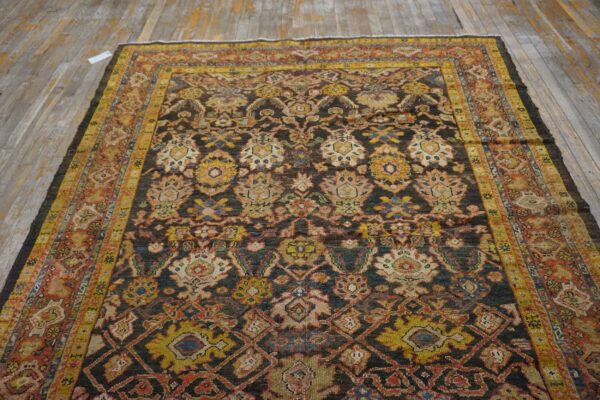 Dark traditional rug featuring complex gold, rust, and cream patterns on a faded wooden floor.