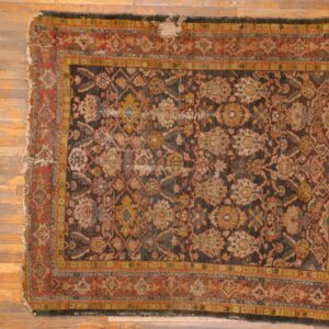 Distressed low-pile rug with complex multicolored traditional pattern on a dark field over wood floors.