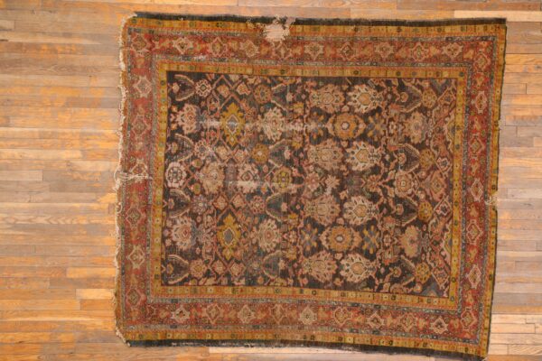 Distressed low-pile rug with complex multicolored traditional pattern on a dark field over wood floors.