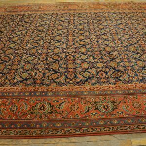 Navy rug with dense repeating orange, red, and green paisley motifs, framed by a wide terracotta border on wood flooring.