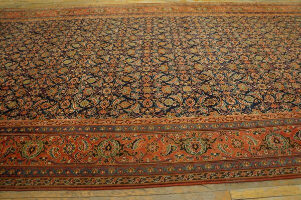 Navy rug with dense repeating orange, red, and green paisley motifs, framed by a wide terracotta border on wood flooring.
