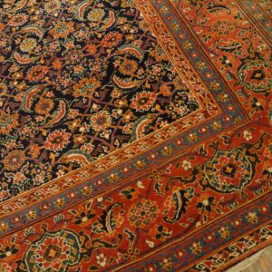 Detail of a patterned rug with a red border and a dark blue field on distressed wood floor.