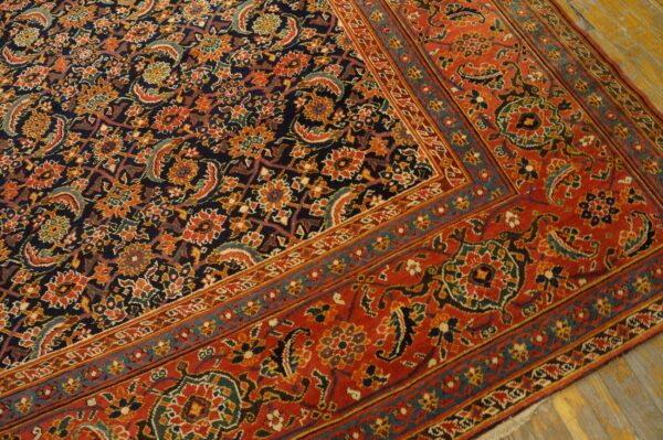 Detail of a patterned rug with a red border and a dark blue field on distressed wood floor.