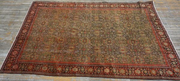 A low-pile rug with a dense gold and rust floral pattern, laid on distressed gray wood flooring.