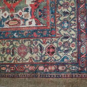 Muted low-pile rug corner displaying complex geometric patterns in red, teal, and khaki beige.