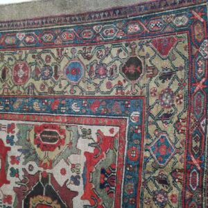 Intricate rug detail featuring a tan field, multiple red and blue geometric borders, and visible fringe on the edge.