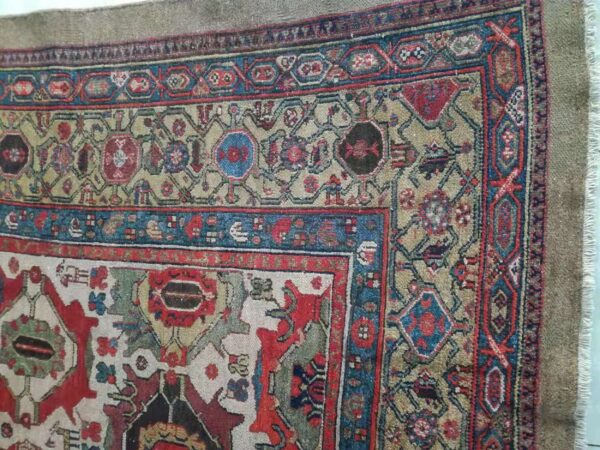 Intricate rug detail featuring a tan field, multiple red and blue geometric borders, and visible fringe on the edge.