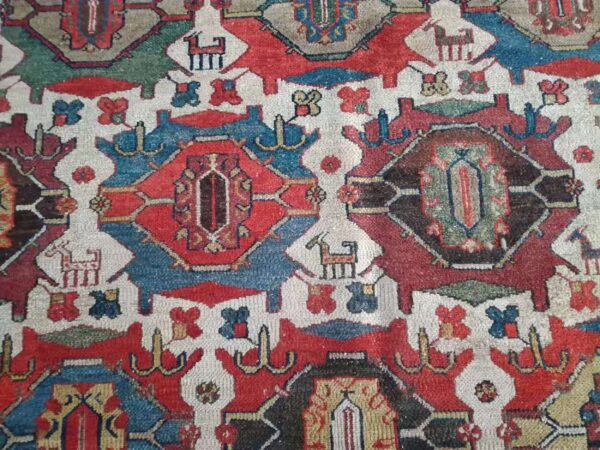 Red, blue, and ivory close-up detail of a medium-pile rug with stylized geometric and animal motifs.