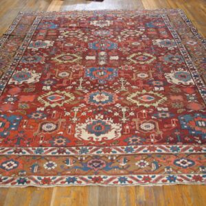 Traditional deep red rug with blue, cream, and tan tribal geometric motifs lying on wood floors.