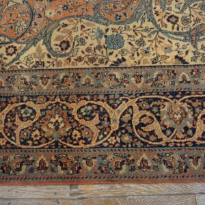 Detail of an intricate floral rug border in navy, rust, and light blue lying over weathered wood floors.