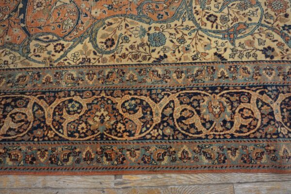 Detail of an intricate floral rug border in navy, rust, and light blue lying over weathered wood floors.
