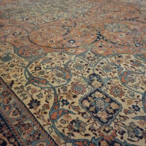 Ornate floral rug pattern in muted coral, beige, navy, and light blue from a low angle.