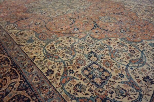 Ornate floral rug pattern in muted coral, beige, navy, and light blue from a low angle.
