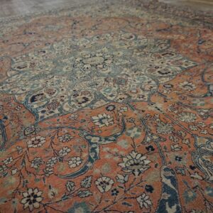 Angled view of a complex, faded traditional rug in orange-red, pale blue, and cream on wood flooring.