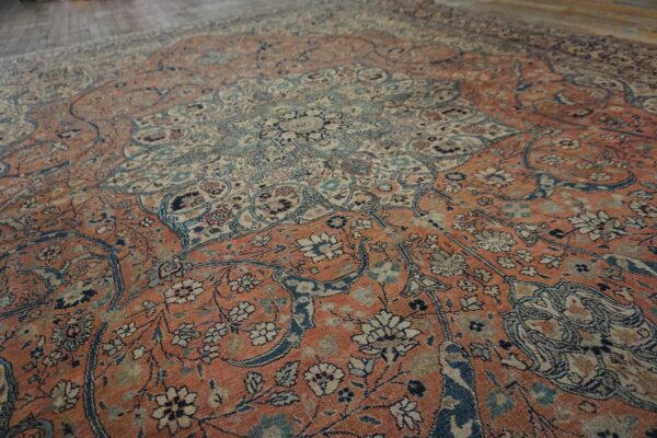 Angled view of a complex, faded traditional rug in orange-red, pale blue, and cream on wood flooring.
