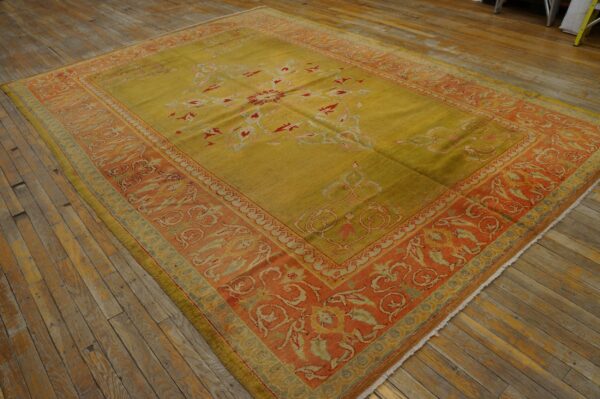 Low-pile rug in golden chartreuse and terracotta tones with scrolling floral motifs on distressed wood.