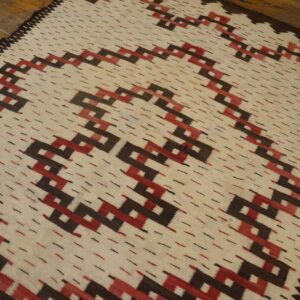 Cream flatweave rug featuring a repeating geometric zig-zag pattern in dark brown and red on a wood floor.