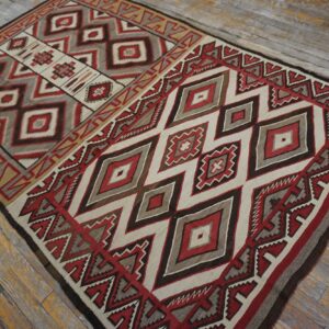 A geometric flatweave rug in red, cream, gray, and dark brown lies on distressed wooden plank flooring.