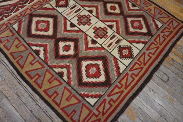 Geometric flatweave rug in red, cream, brown, and grey with a diamond center and arrow motifs on worn wood floor.