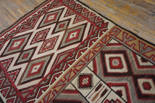 Geometric flat rug with red, cream, brown, and gray diamond patterns on worn wood flooring.