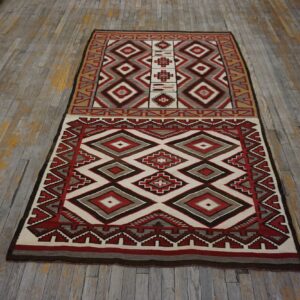 Flat-woven rug featuring red, cream, gray, and brown geometric diamonds on rustic hardwood flooring.