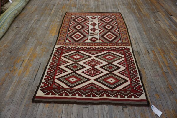 Flat-woven rug featuring red, cream, gray, and brown geometric diamonds on rustic hardwood flooring.