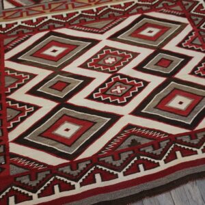 Geometric rug in red, white, gray, and brown with nested diamonds, lying on distressed gray wood planking.
