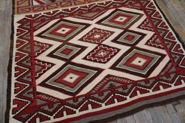 Geometric rug in red, white, gray, and brown with nested diamonds, lying on distressed gray wood planking.