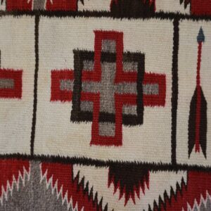 Flatweave rug detail with red, brown, and gray geometric crosses and arrow designs on a cream ground.