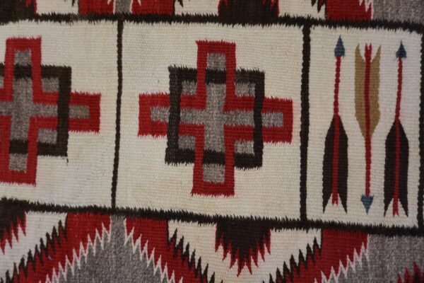 Flatweave rug detail with red, brown, and gray geometric crosses and arrow designs on a cream ground.
