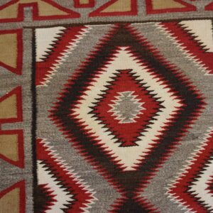 Geometric flatweave rug detail in red, white, grey, and tan with large zig-zag diamond motifs.