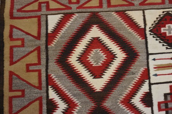 Geometric flatweave rug detail in red, white, grey, and tan with large zig-zag diamond motifs.