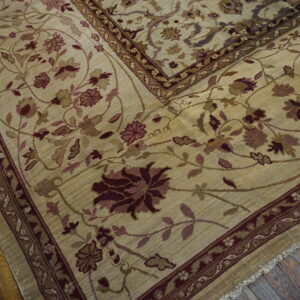 Large beige area rug featuring low pile and traditional dense floral designs in deep purple and gold.