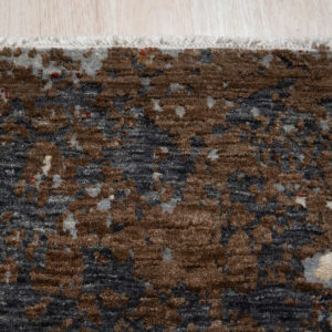 Close-up of a blue-gray, rust, and white textured abstract rug lying on light wood flooring.