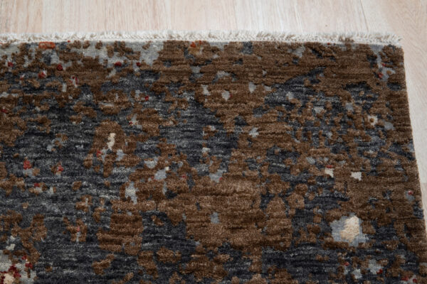 Close-up of a blue-gray, rust, and white textured abstract rug lying on light wood flooring.