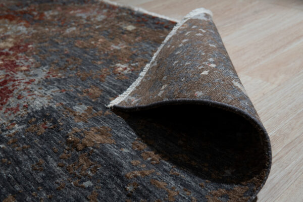 Textured dark brown and gray abstract rug pile detail with white fringe on light wooden planks.