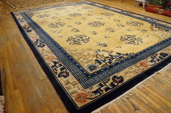 Large yellow rug with dark blue borders and stylized floral medallions on distressed wooden plank flooring.