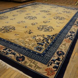 Golden yellow rug featuring scattered blue floral motifs and wide geometric navy and beige borders on wood flooring.