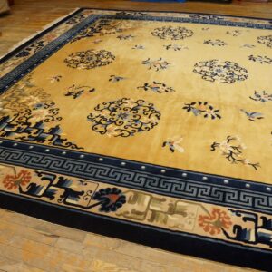 Gold rug with a dark blue Greek key border and scattered blue and cream floral motifs on wood flooring.