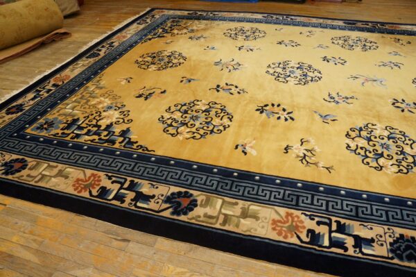 Gold rug with a dark blue greek key border and scattered blue and cream floral motifs on wood flooring.