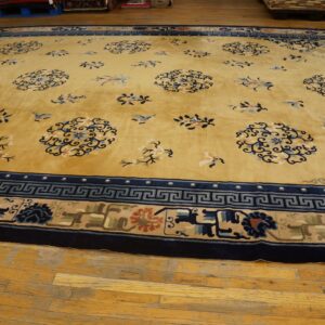 Large golden yellow rug featuring scattered blue floral motifs and multi-color borders on wood planks.