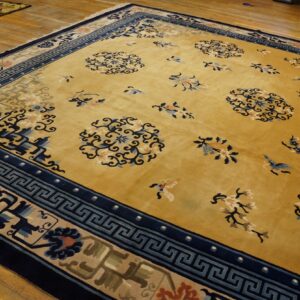 Mustard yellow rug with navy Greek key and floral borders, featuring light blue medallions on wood flooring.