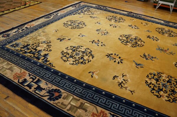 Mustard yellow rug with navy greek key and floral borders, featuring light blue medallions on wood flooring.