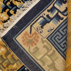 Blue, gold, and tan patterned rug is folded over, revealing the woven backing and fringe on wood flooring.